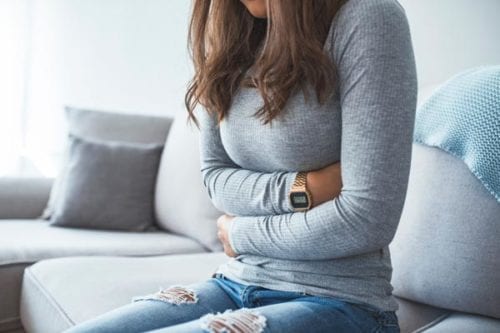 Teenage girl holding mid section after irregular menstruation symptoms are treated by Dr. Joshua Smith, a pediatric endocrinologist in Pocatello and Idaho Falls.